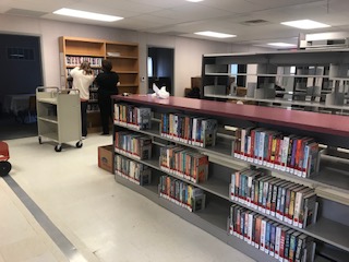 Sets of bookshelves. Caucasian man and African American woman in background placing books on shelf.