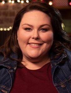 Chrissy Metz, young Caucasian woman with burgundy blouse and denim jacket, smiling.