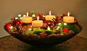 bowl with Christmas ornaments, pine cones, moss and candles on a carved wooden table