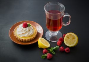 tart on brown plate next to cider in glass mug, lemon halves and raspberries