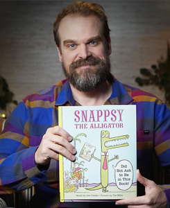 Caucasian male with mustache and beard holding up a children's book.
