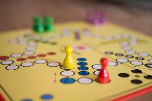 closeup of board game with multicolored pegs and yellow board with paths of multicolored circles and a red border.